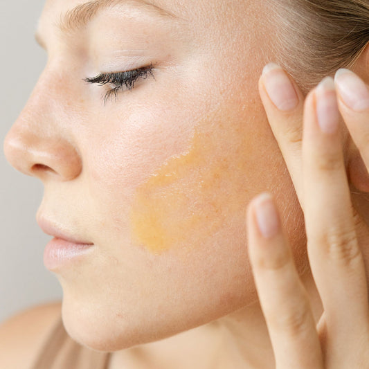 Woman applying a cosmetic product to her face with a neutral background