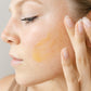 Woman applying a cosmetic product to her face with a neutral background