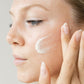 Woman applying cream to her face with a neutral background