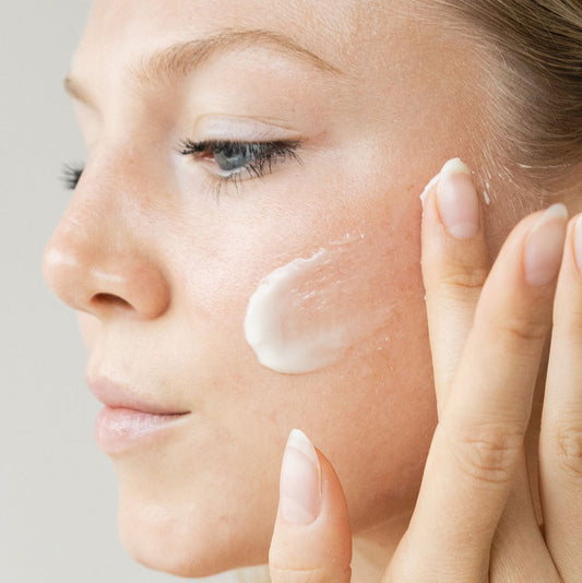 Woman applying cream to her face with a neutral background