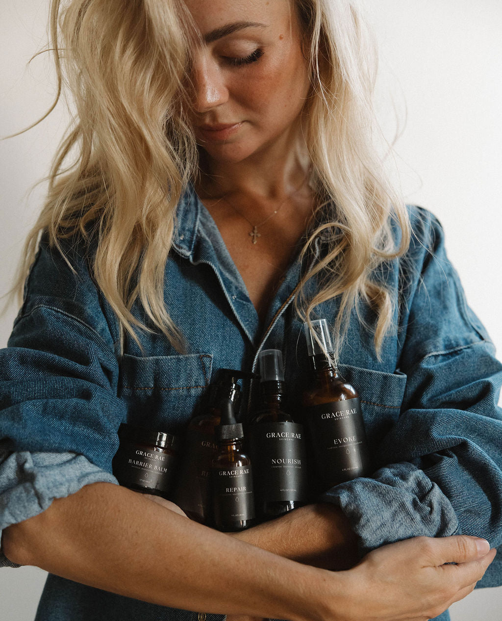 Woman holding several dark glass bottles against a neutral background