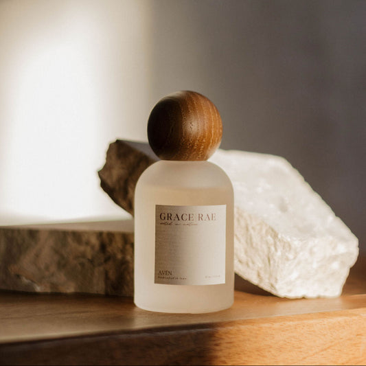 Bottle of Grace | Rae perfume with wooden cap on a wooden surface with a blurred background